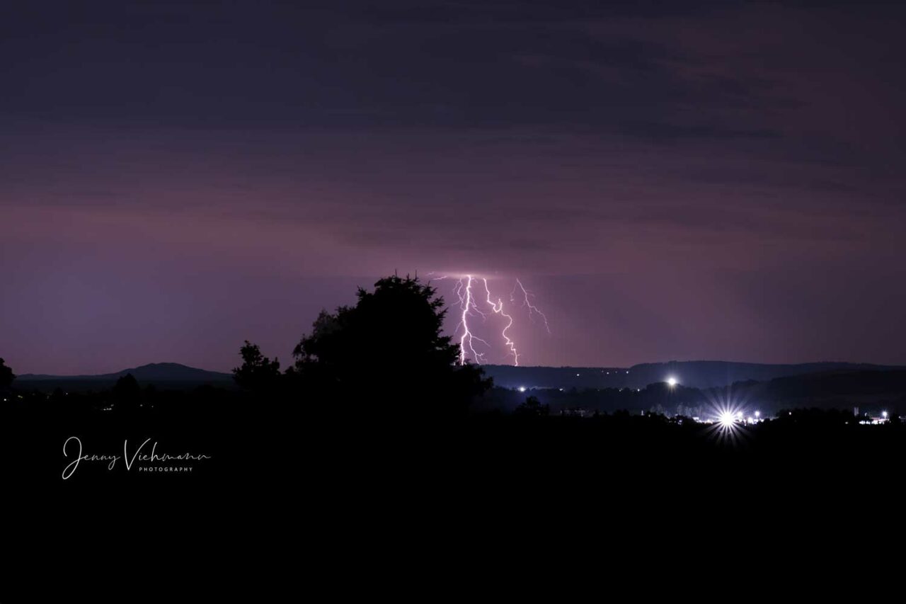 Nachtszene mit einem dramatischen Blitz, der den Himmel über einer ländlichen Landschaft erleuchtet.