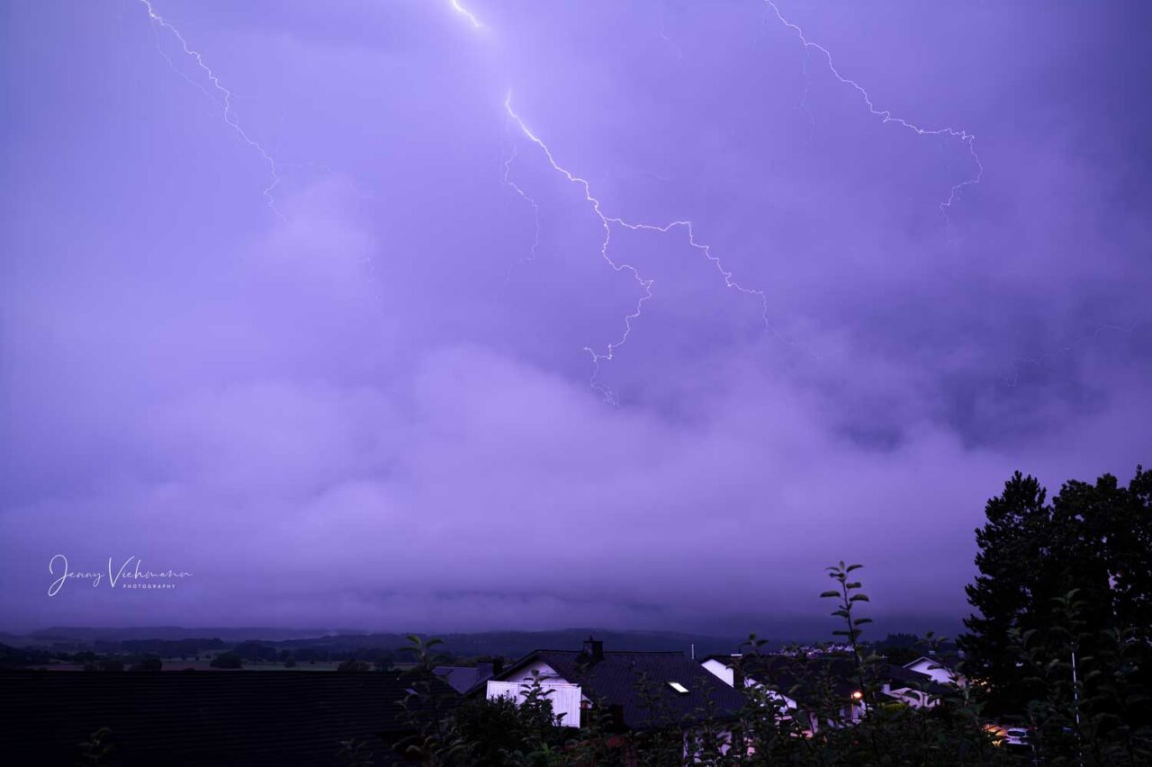 Nachtszene mit einem dramatischen Blitz, der den Himmel über einer ländlichen Landschaft erleuchtet.